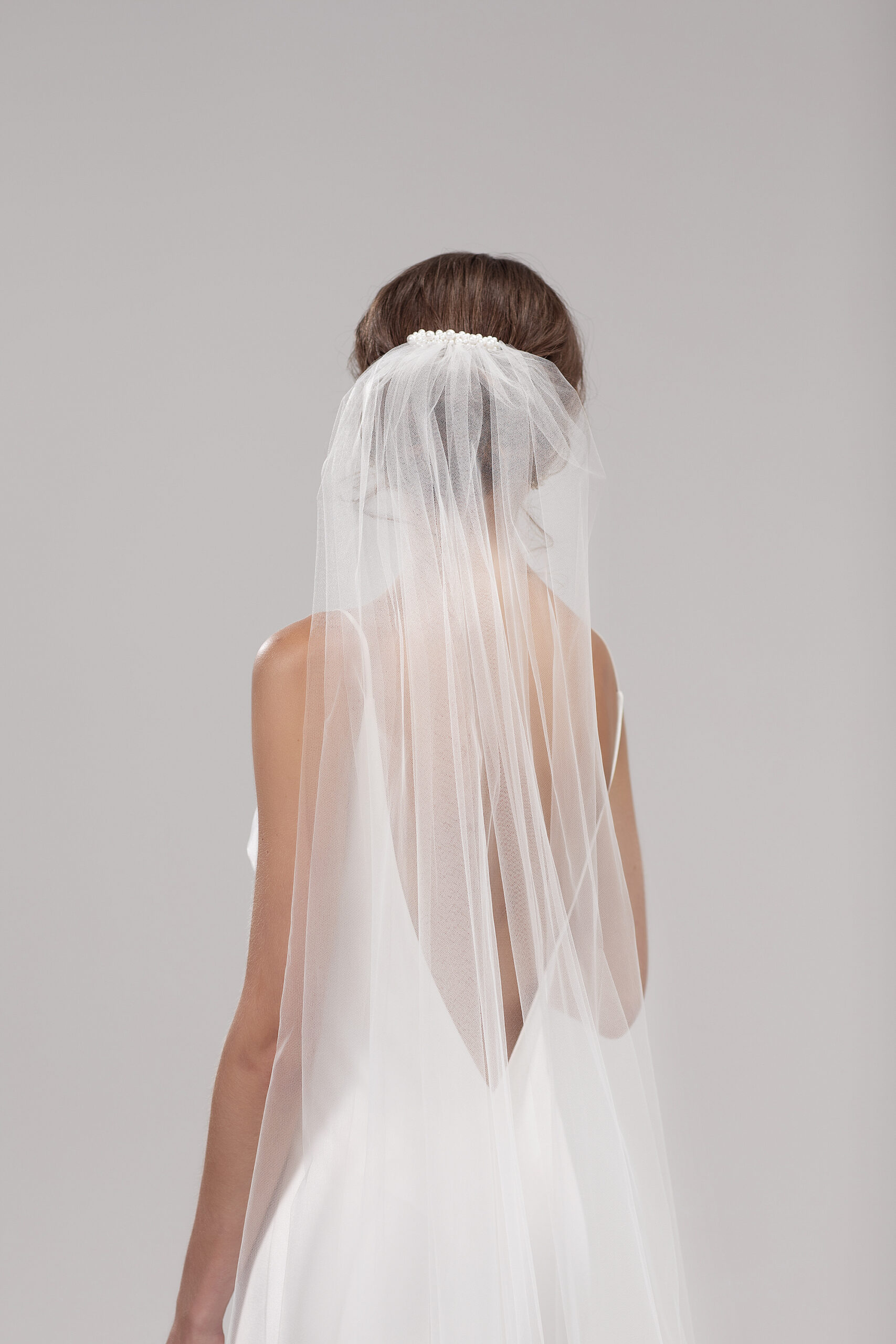 Back view of model wearing the Lily veil gathered above a low bun. Lily is a single layer 2.5m veil with a pearl comb.
