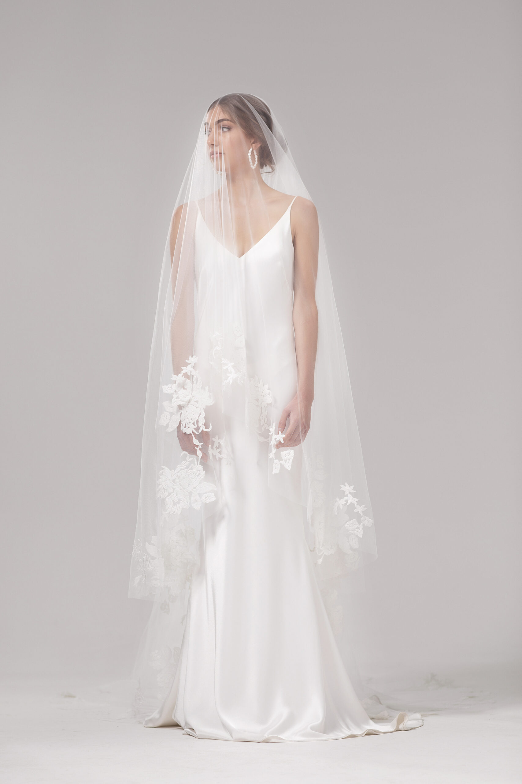 Front view of model wearing the Mayfair veil blusher style over the face. Mayfair is a two-tier 2.5m veil with delicate floral embroidery around the edge.