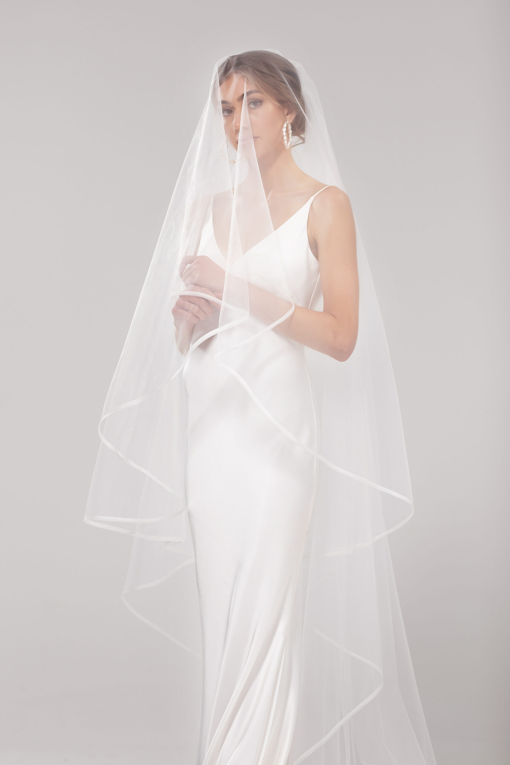 Front view of model wearing Snow blusher style, with one tier over the face. Snow is a 2.5m two-tier blusher style veil with an organza binding on the edge.