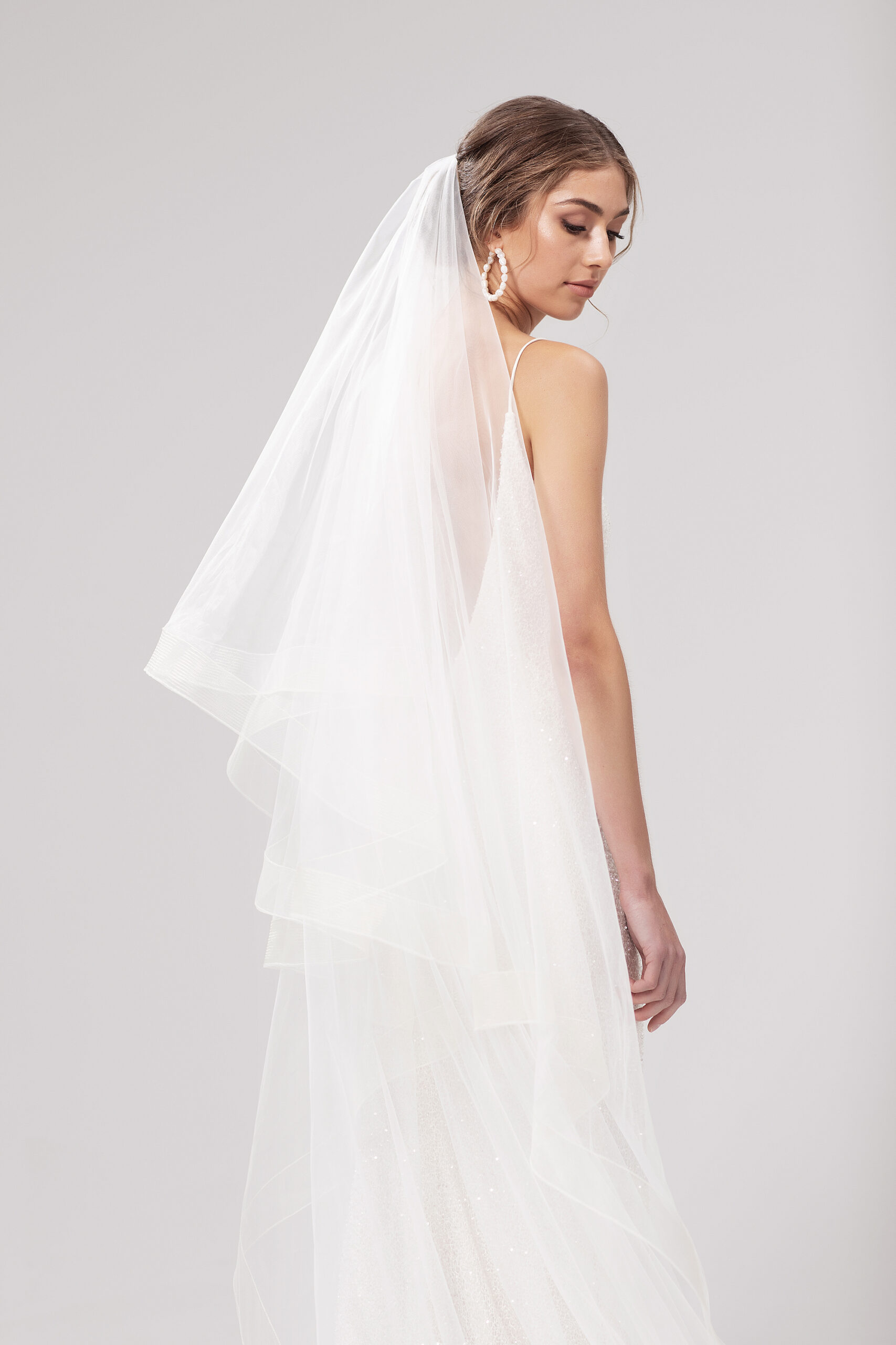 Back view of model wearing Tess over a low bun, with both tiers sitting behind. Tess is a 2.5m two-tier blusher veil with a 5cm trim around the edge.
