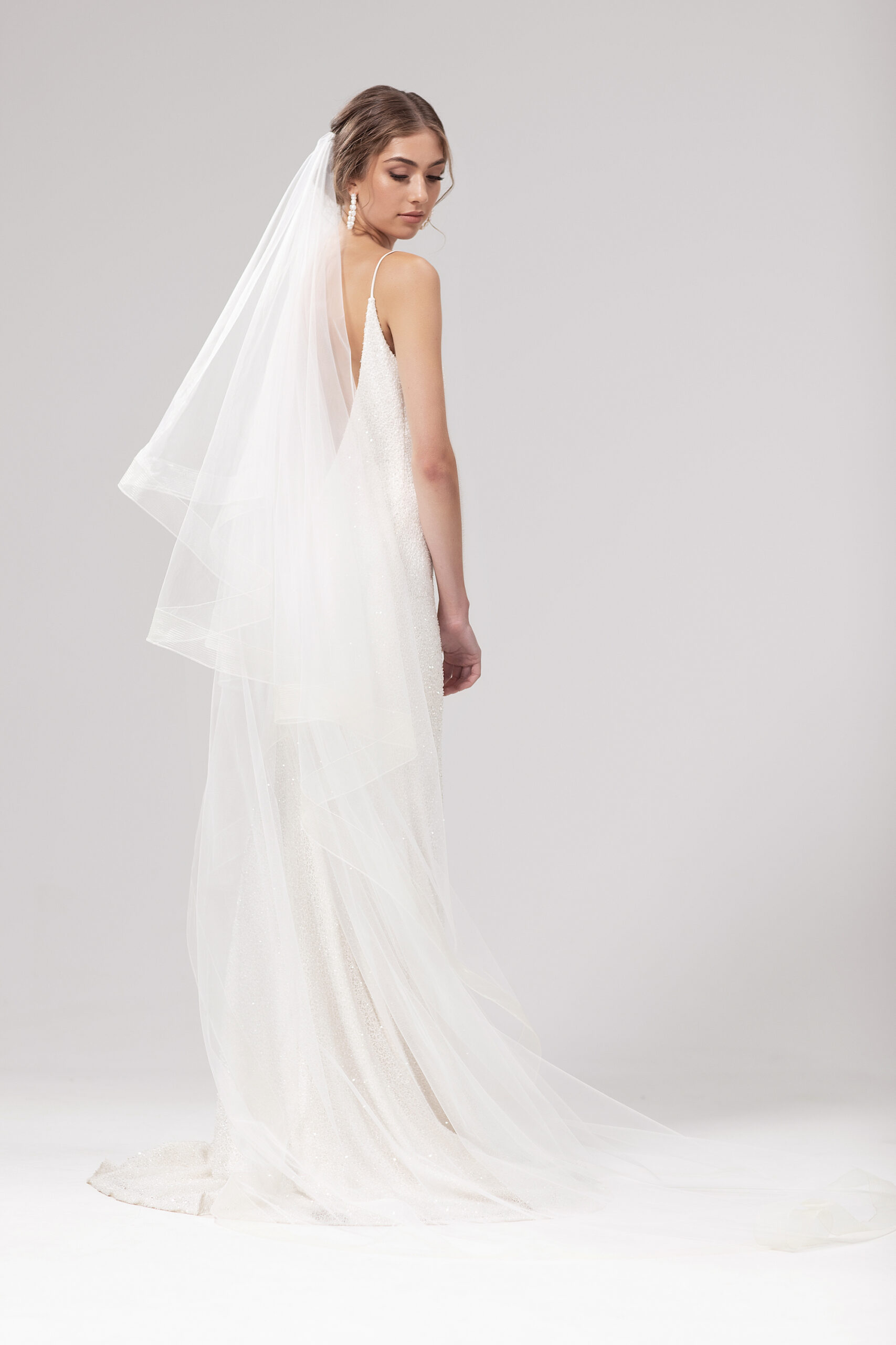 Back view of model wearing Tess with both tiers behind. Tess is a 2.5m two-tier blusher veil with a 5cm trim around the edge.