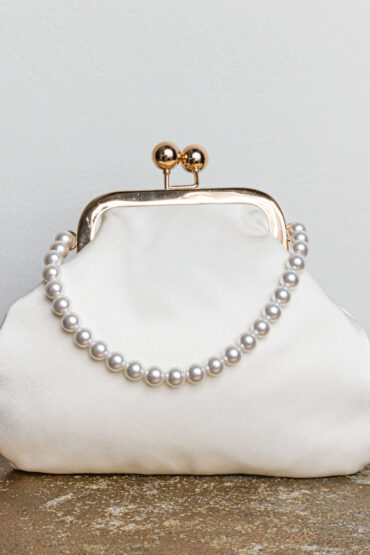 A sleek satin clutch featuring a pearl strap and fastened with a gold kiss-lock.