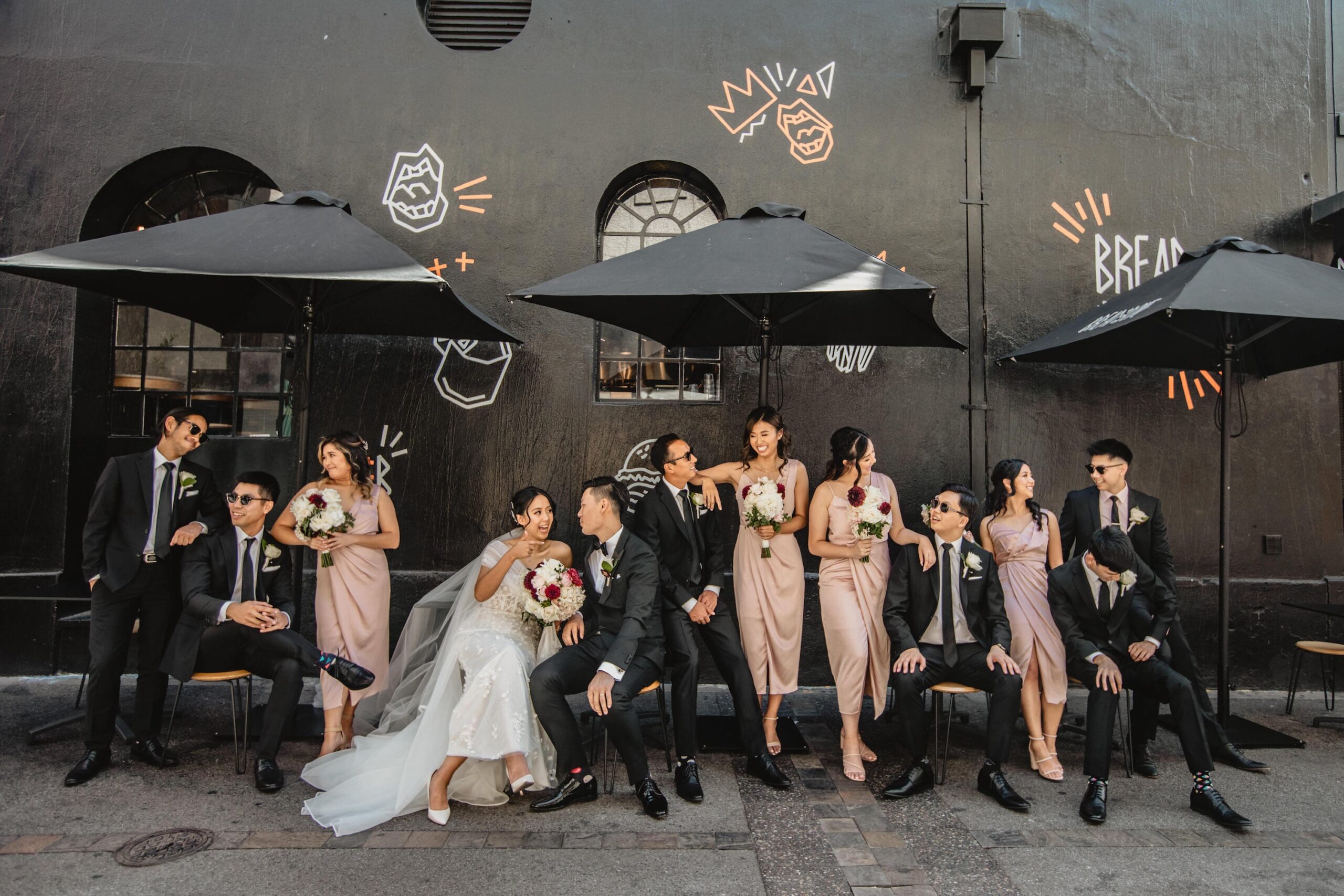 Calèche Real Bride Anita & Terence - bridal party siting and standing outside restaurant wall in city laneway