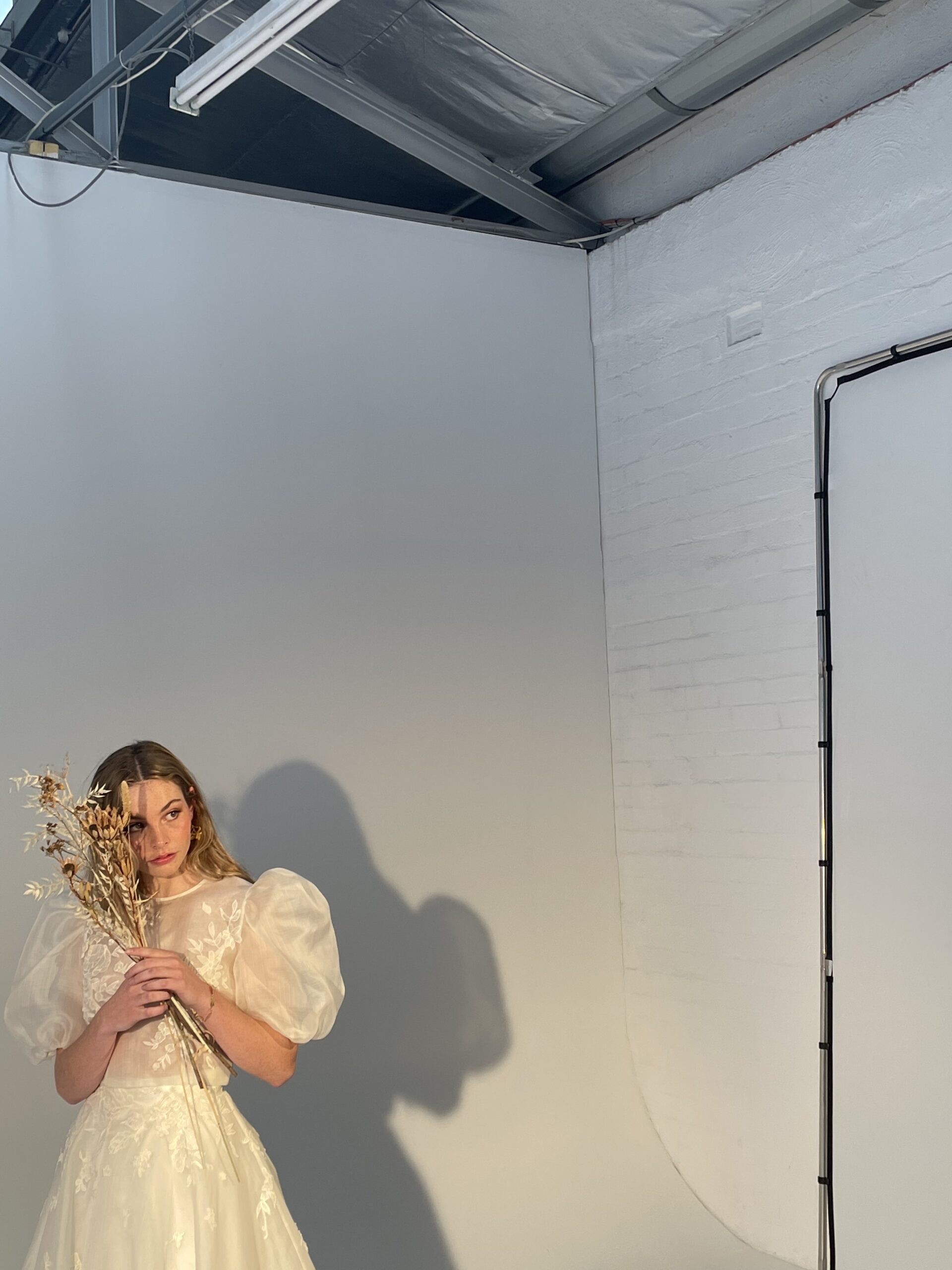Model jess being photographed holding dried flowers in the elsie and iris gown in the studio