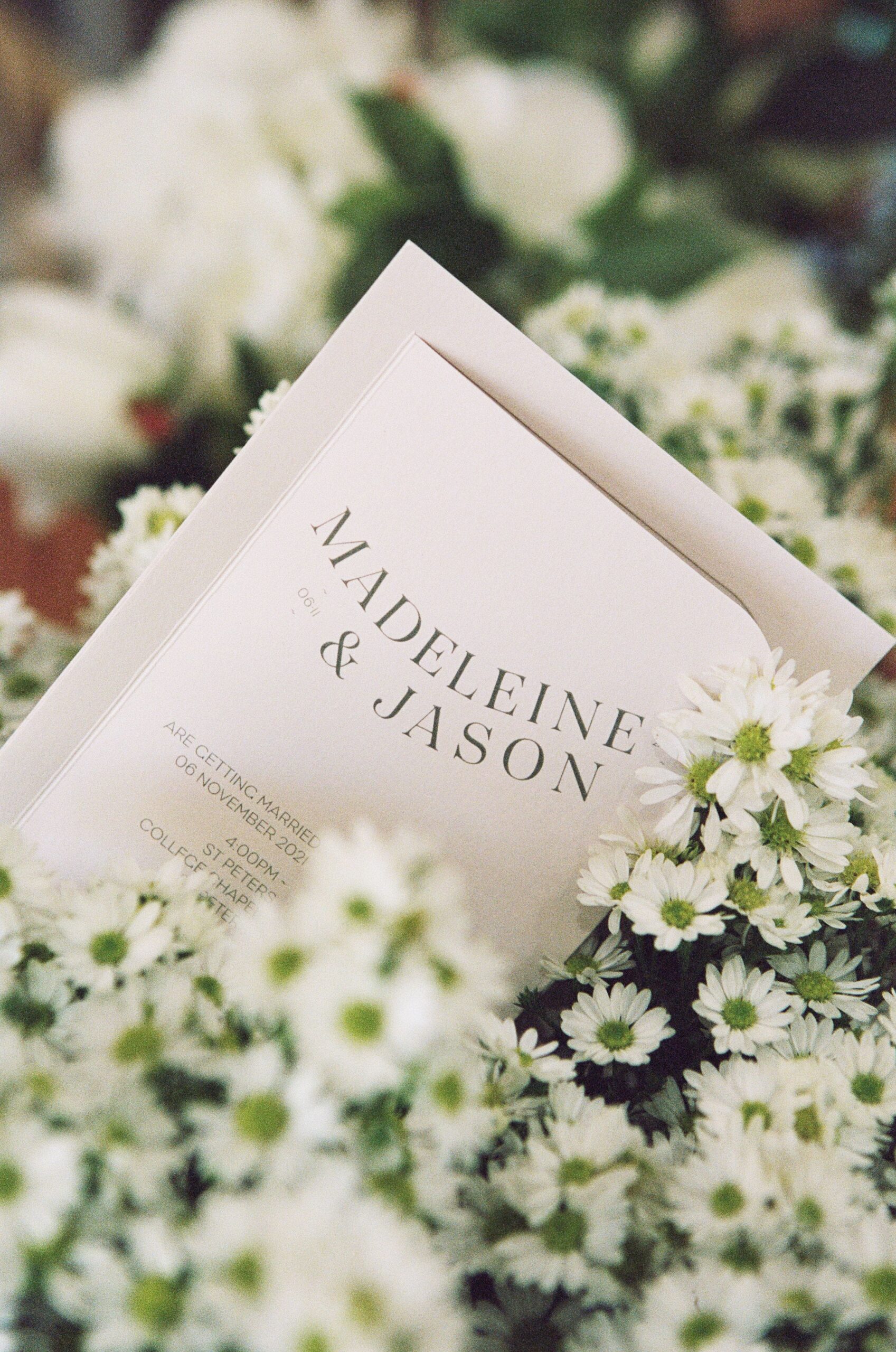 Invite titled Madeleine & Jason sitting amongst white flowers