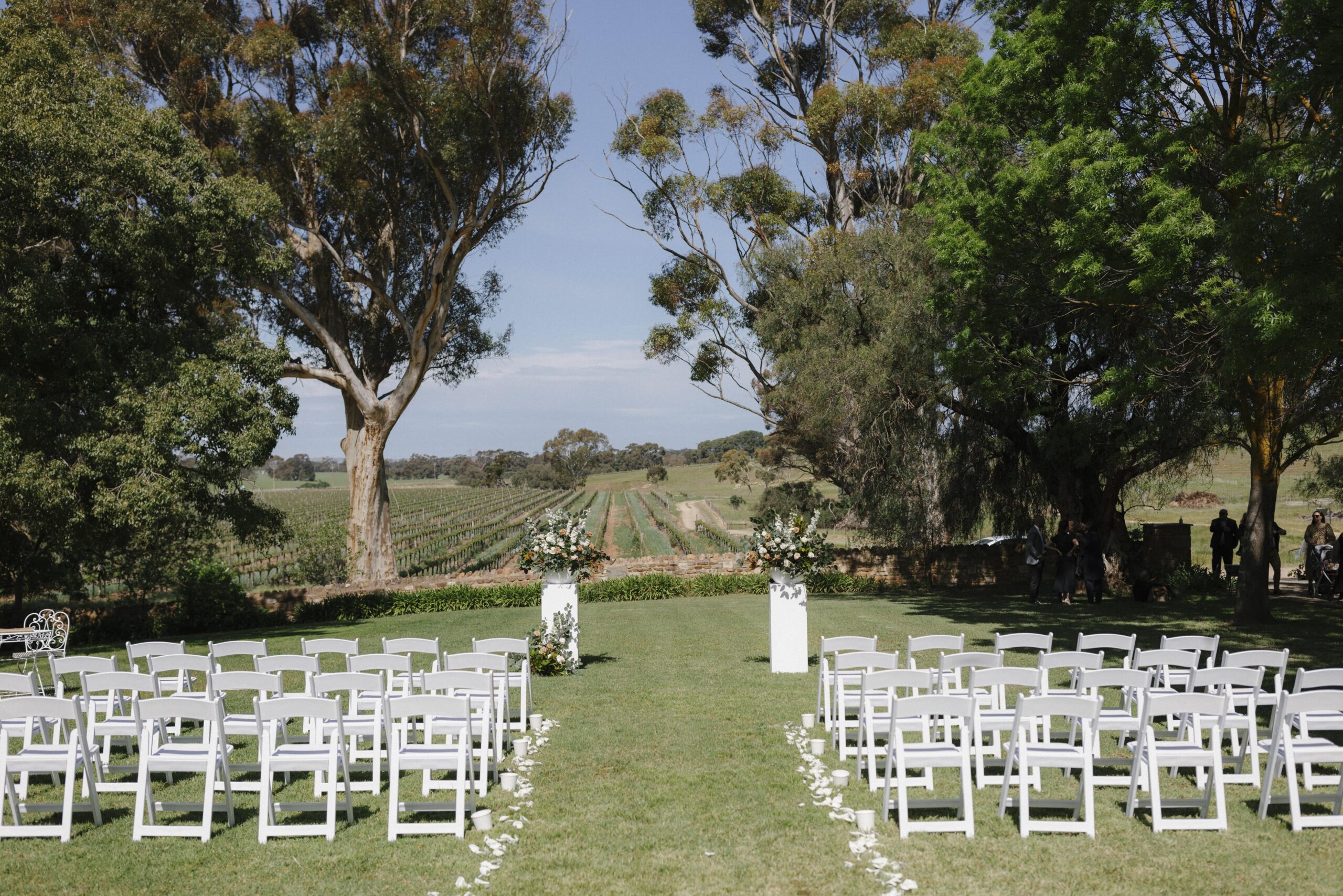 Ceremony - white chairs and white flower petals amongst green trees and vineyards