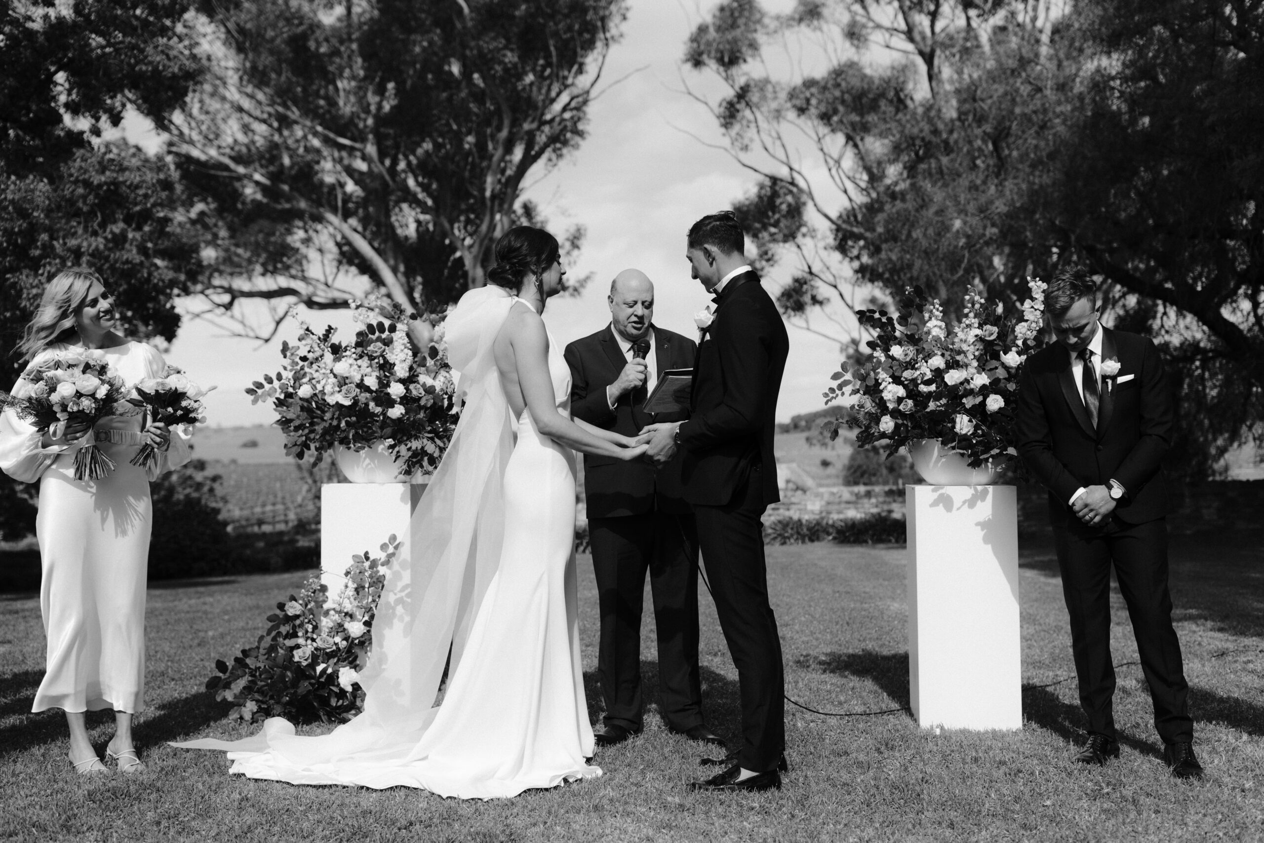 A black and white image of Olivia and Patrick standing hand in hand exchanging vows