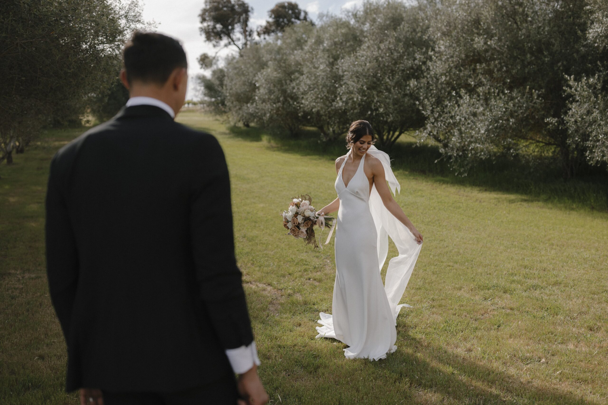 Olivia showing off her gown to Patrick amongst a backdrop of olive trees and grass