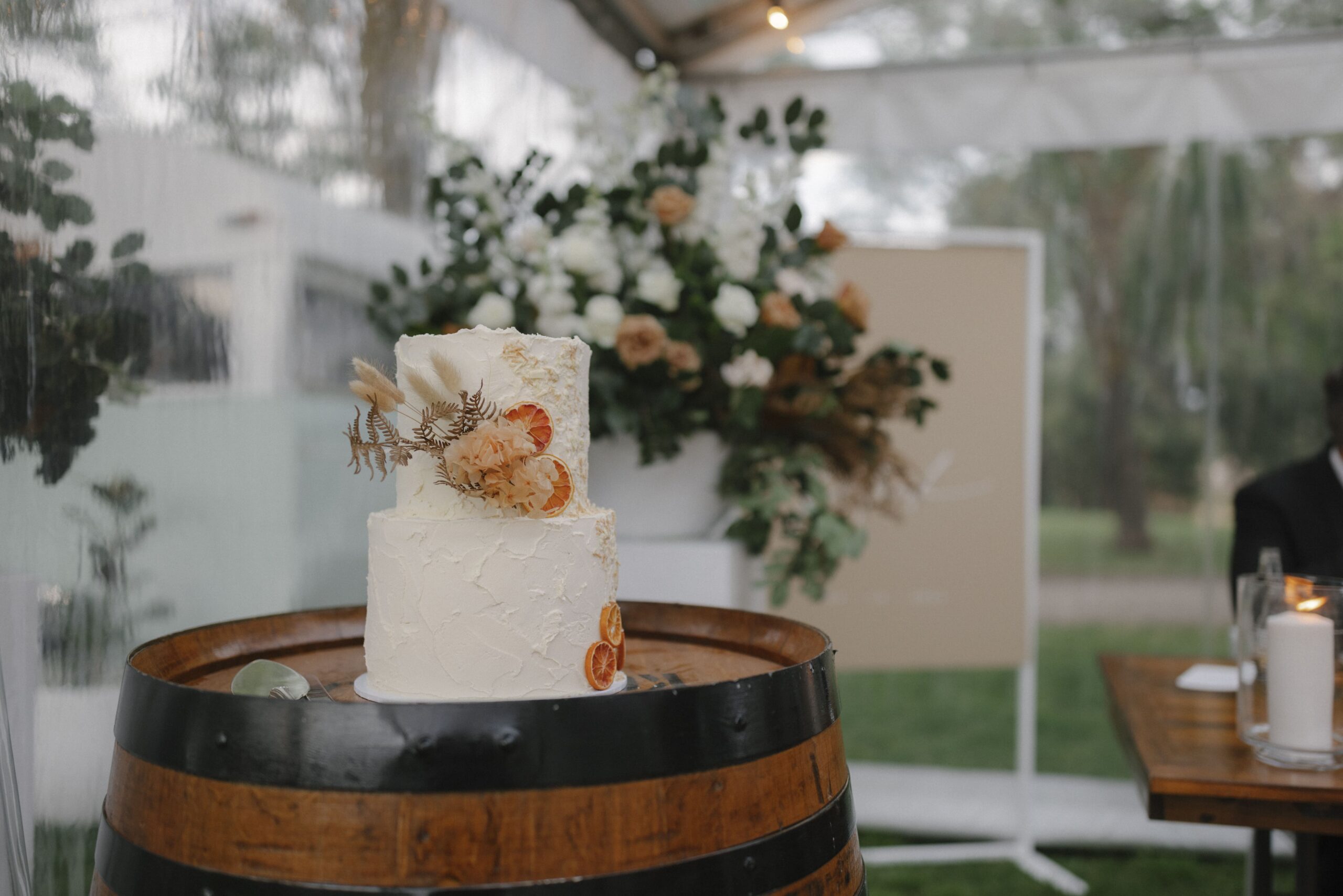 Floral cake sitting on a wine barrel with floral decor in the background