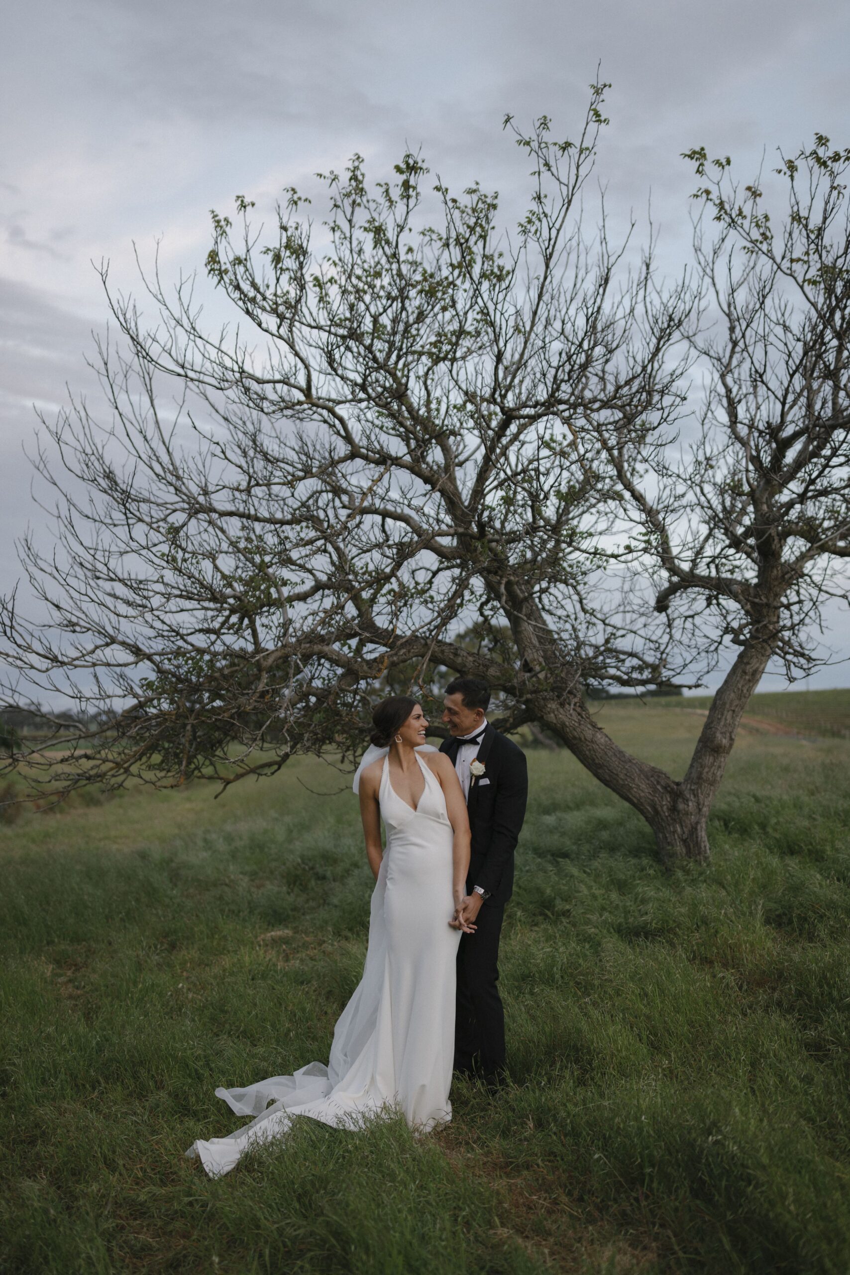 Olivia and Patrick standing under a bare tree amongst deep green grass