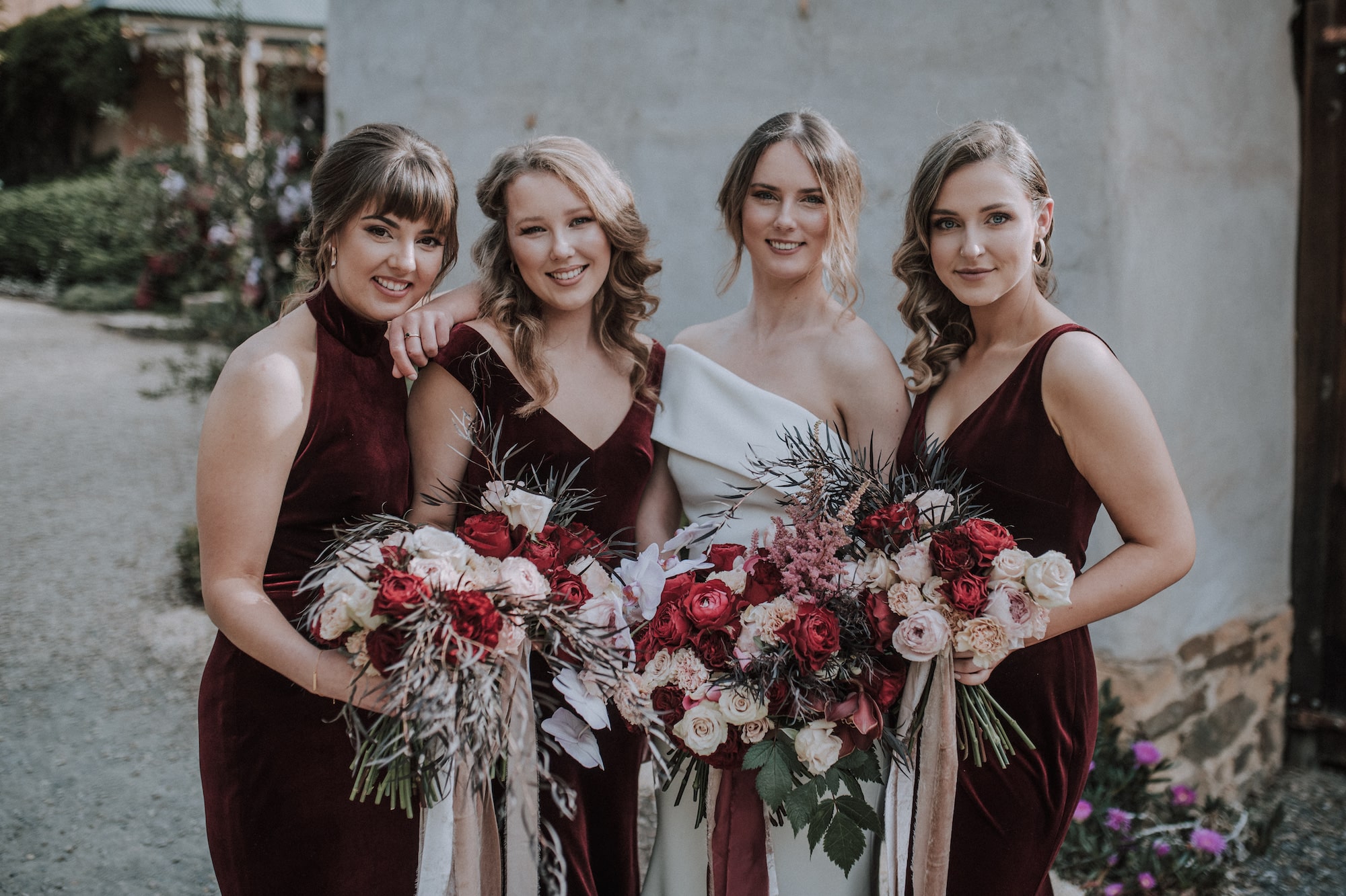 Landscape shot of bride and bridesmaids. Bridesmaids are also wearing 3 different red velvet gowns.