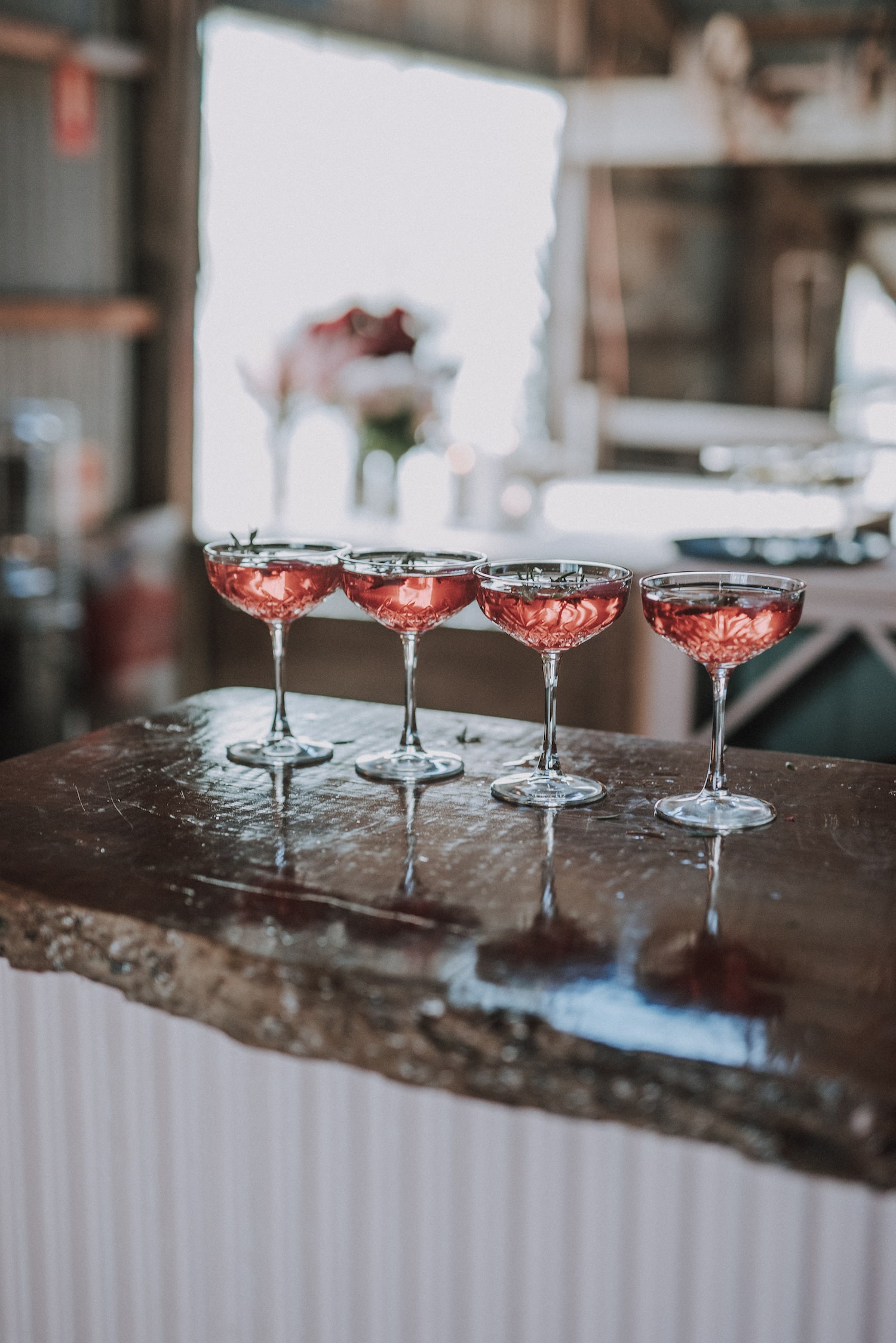 4 pink cocktails lined up on a wooden bar