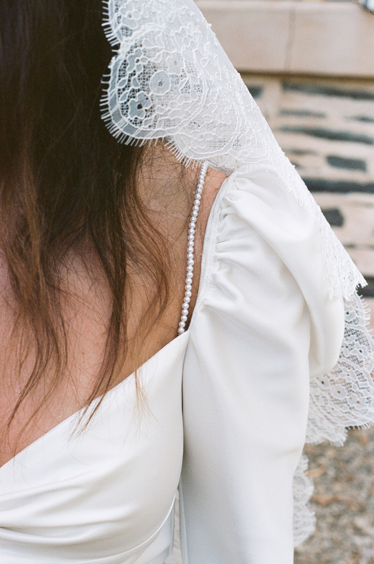 Close up of brides left shoulder and veil. Brides gown has a small pearl strap sitting next to puffed sleeves. The veil is a chantilly lace veil with scallop edging.