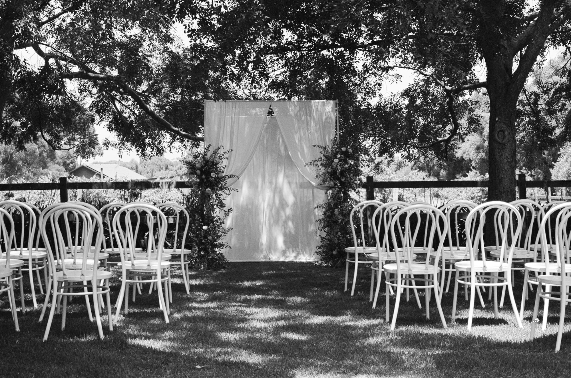 Ceremony - outside with white chairs with a backdrop of hanging white sheets with floral foliage.