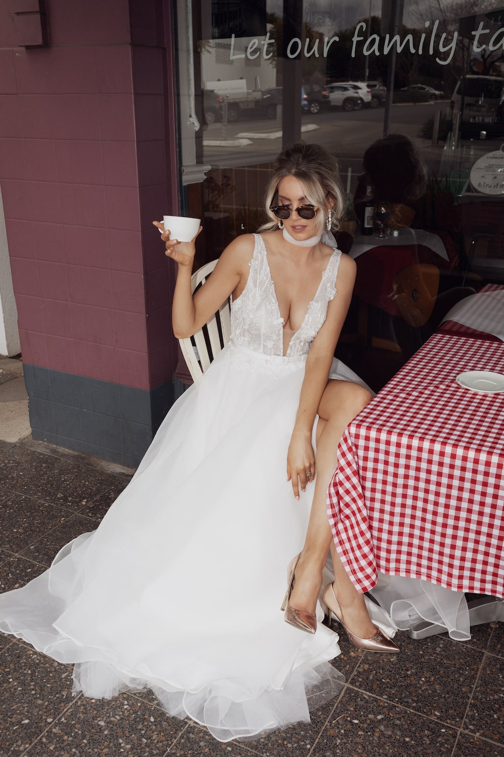 Model sitting on table outside window of cafe wearing the Liliana gown.