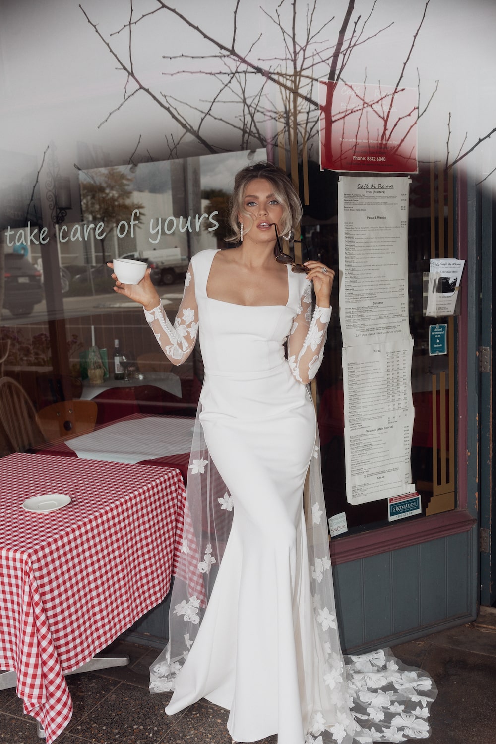 Bride standing outside an Italian cafe with a cup of coffee, wearing the Tivoli gown.