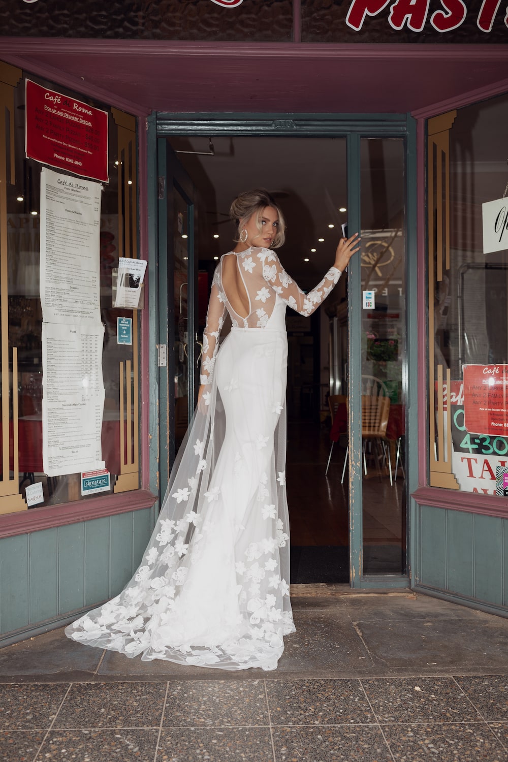 Bride walking through doorway of Italian cafe, looking back at camera, wearing the Tivoli gown.