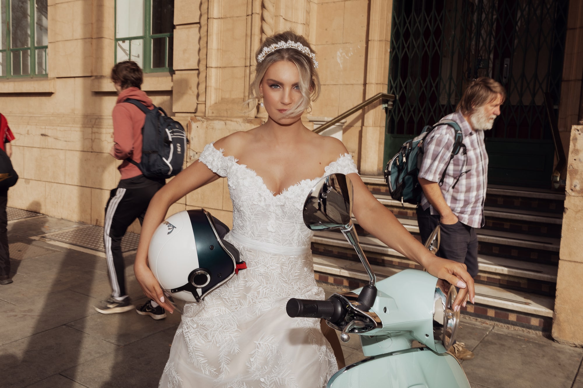 Model sitting on mint green scooter holding a white helmet, facing the camera
