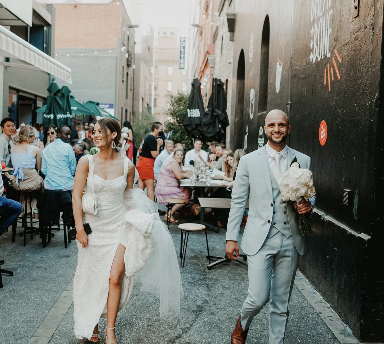Cristiana and Jake walking down a busy city laneway smiling at onlookers