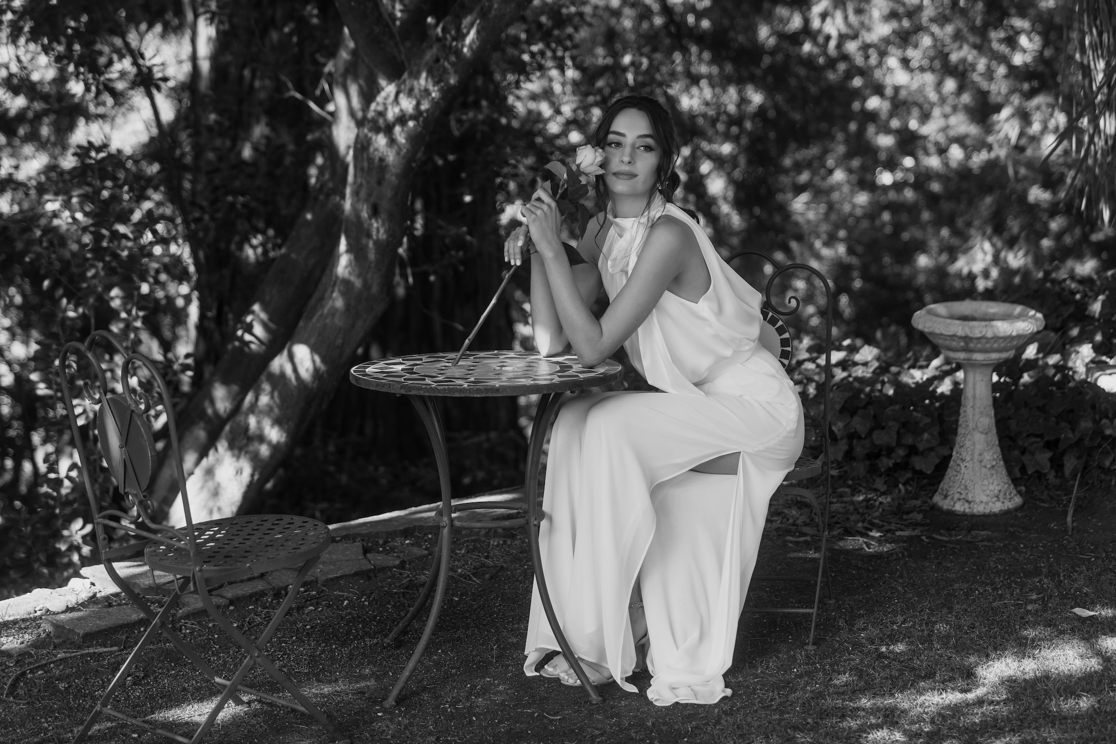 Model sitting at garden table holding rose