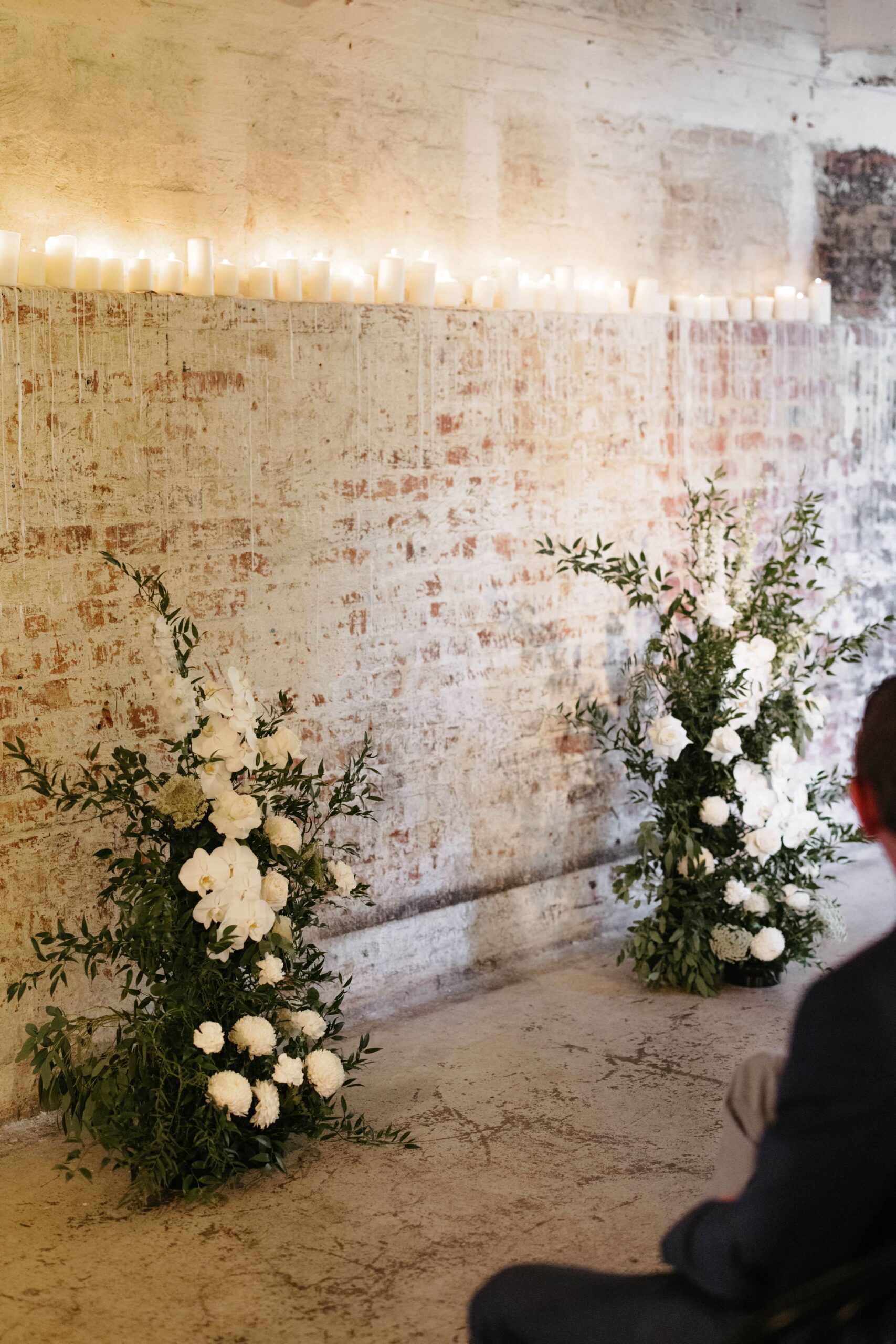 Two freestanding floral arrangements infront of an indoor exposed brick wall for the ceremony