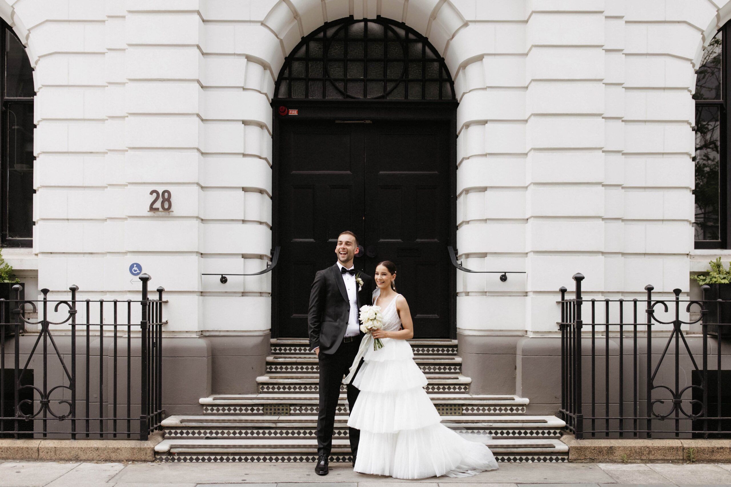 Bethany and Daniel photographed standing in front of a white brick city building