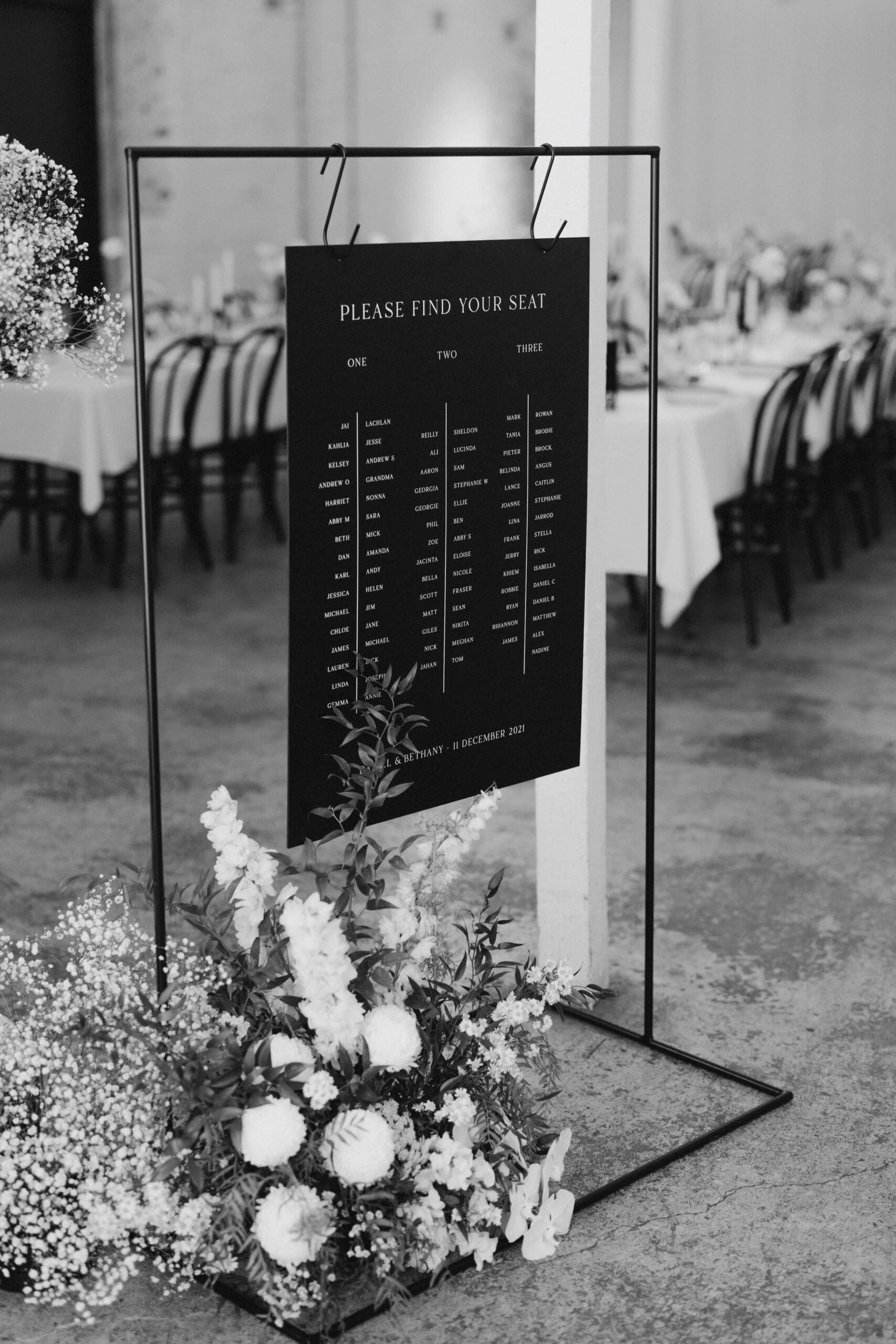 Reception signage - seating arrangement. A black sign with floral arrangement at the base.
