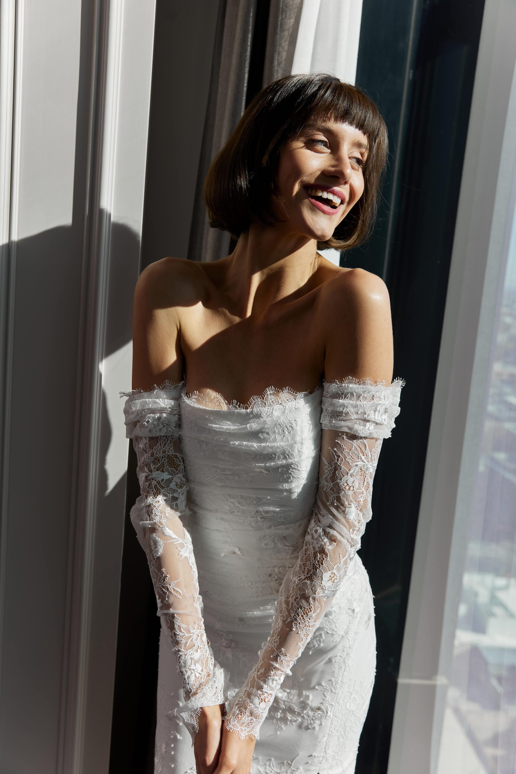 Colette - a strapless soft mermaid gown with a rouched lace overlay and detached sheer sleeves.