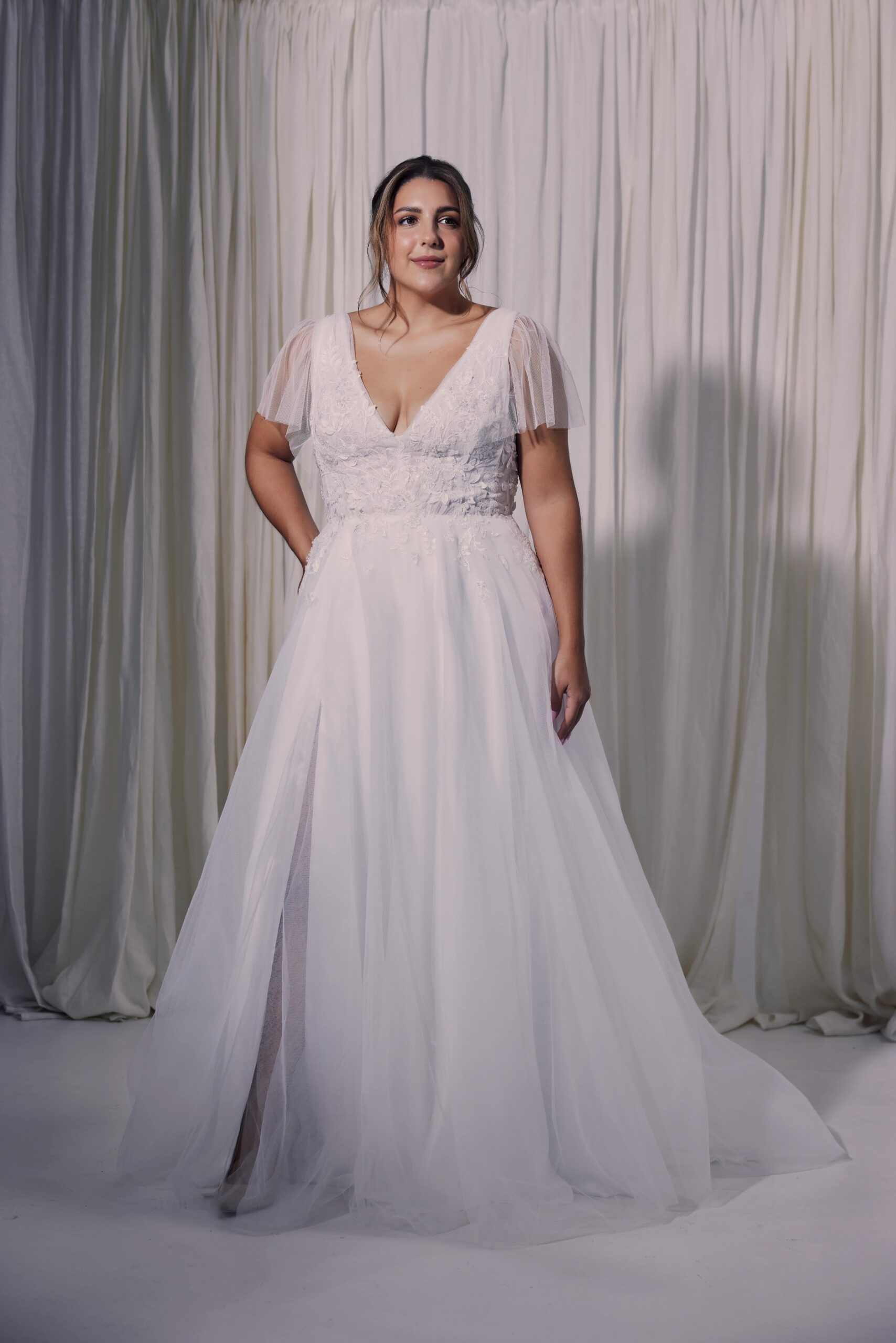 The Ellie gown - a v-neck gown with soft rouched bodice, flutter sleeves and 3D lace applique trailing into a soft flowing skirt.