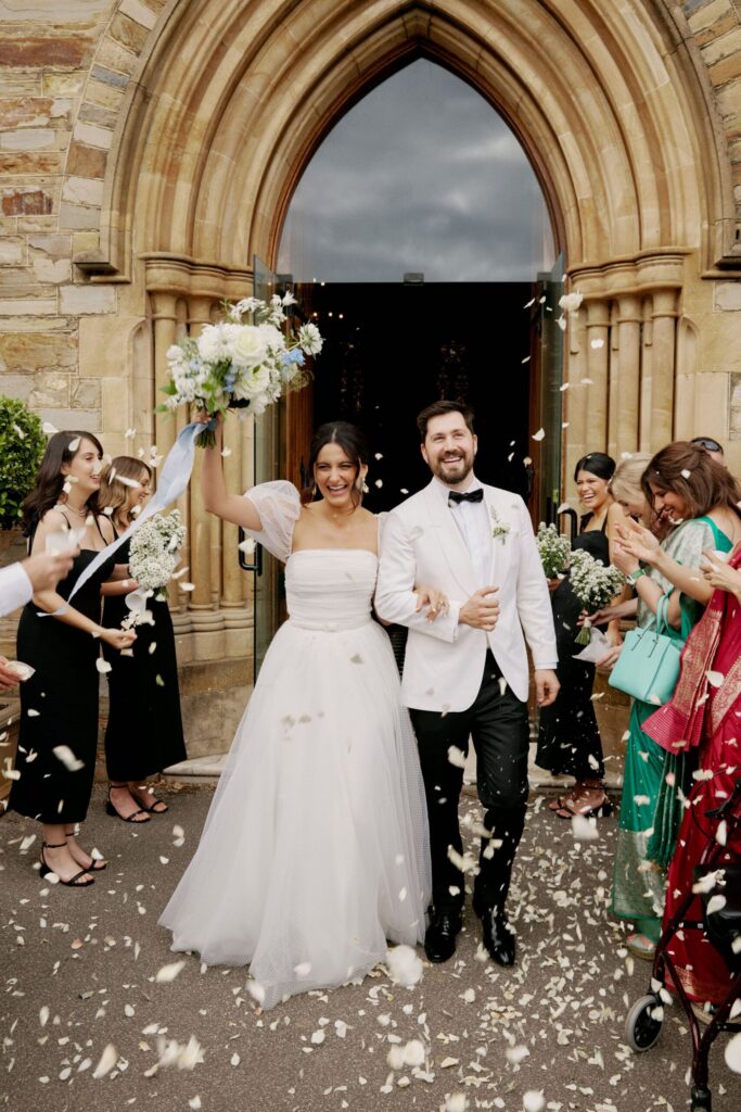 Maddy and Jason walking through flower petals, leaving the church