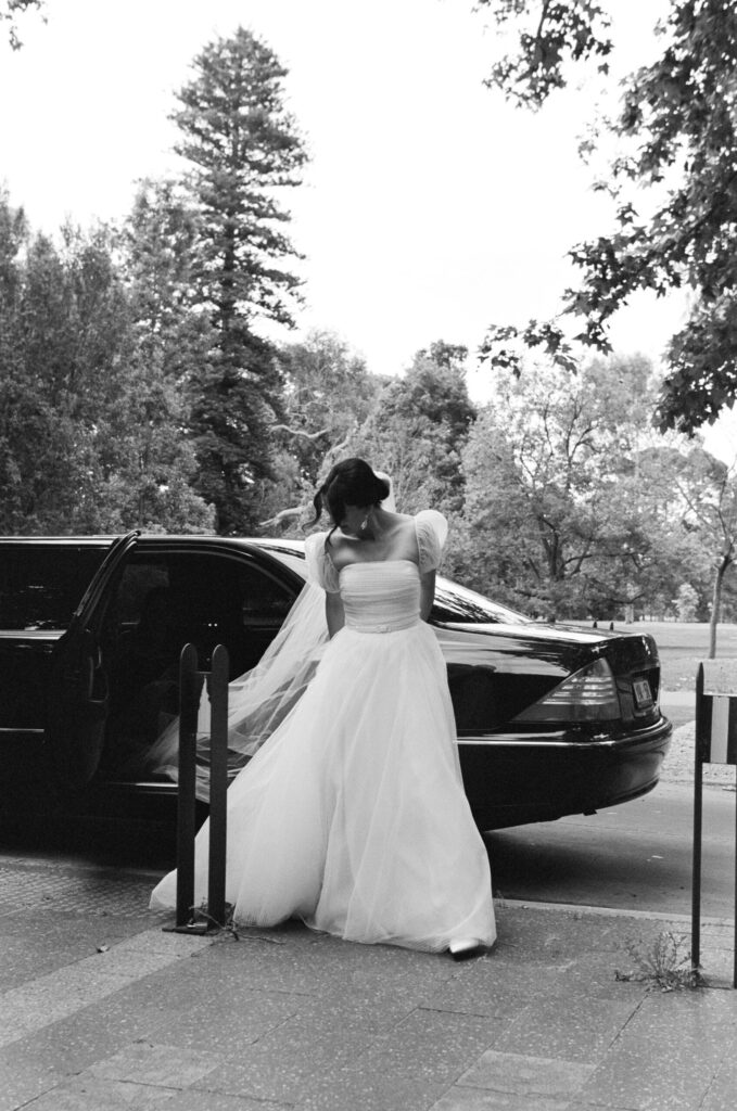 Bride Maddy getting out of car with veil flowing behind"