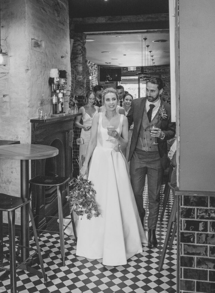 Black and white shot of Maia and Andrew walking through bar torino