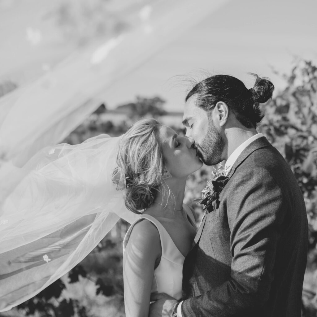 Black and white shot of Maia and Andrew sharing a kiss in the vineyards