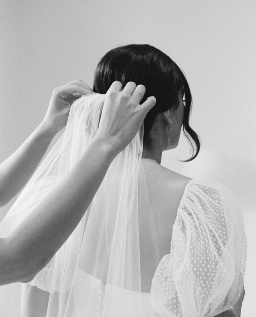 Maddy's bridesmaid inserting a veil into Maddy's hair in black and white