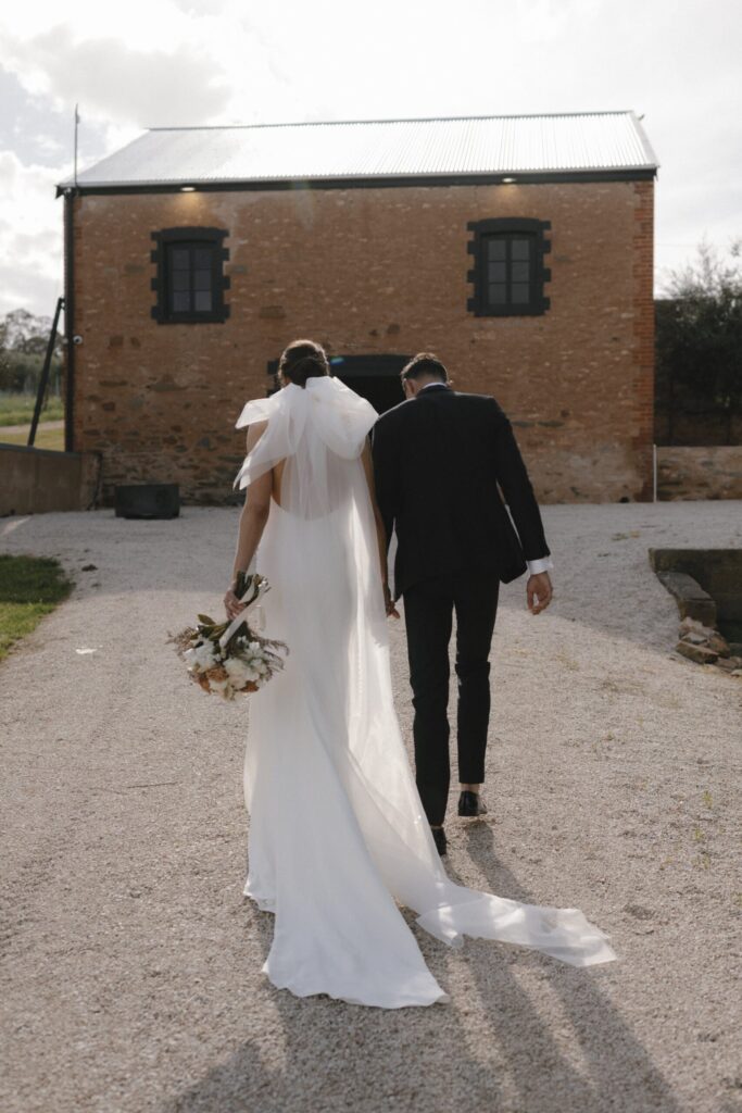 Olivia and Patrick walking hand in hand towards an old red brick building