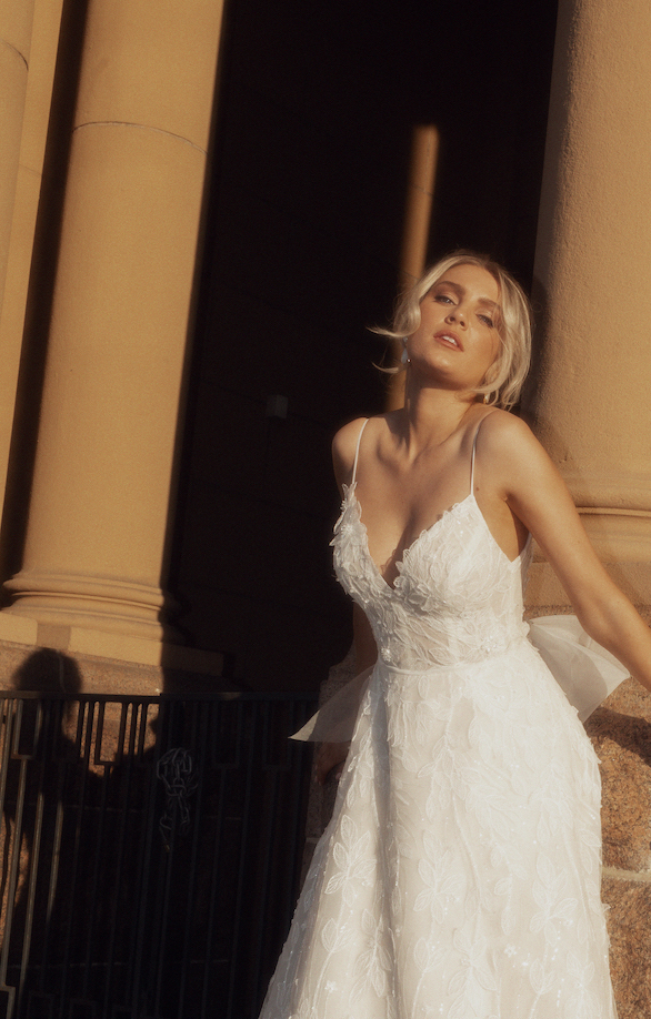 Georgia in the Sinfonia gown leaning against a brick wall