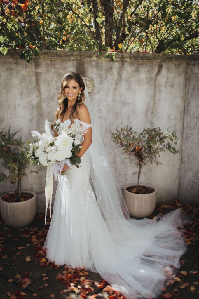 Portrait of Bride Ashley in her figure-hugging lace gown with corset style bodice and off the shoulder sleeves.